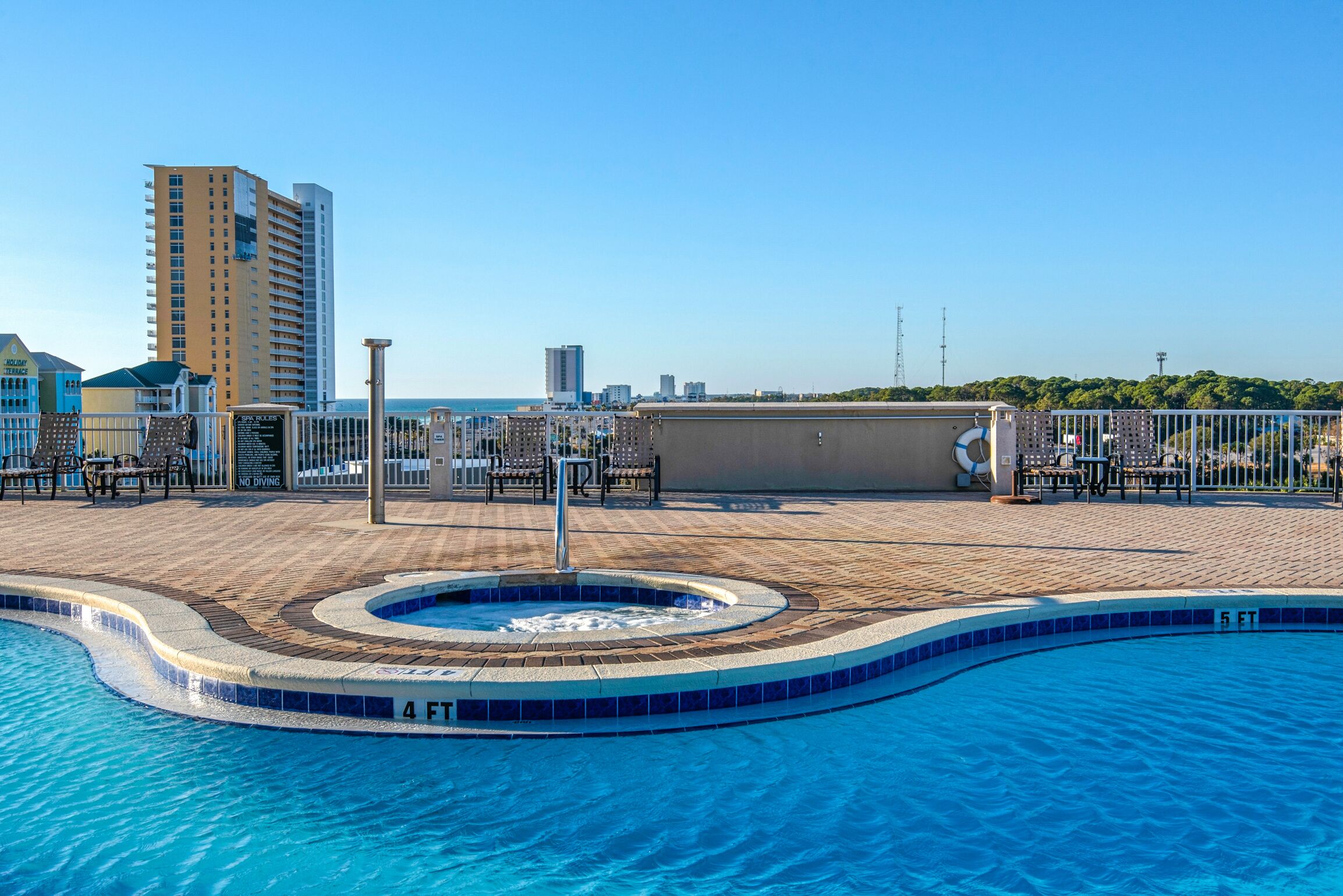 Una piscina en la azotea con un jacuzzi y sillas de descanso, rodeada por un paisaje urbano.
