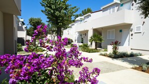 A modern residential building with a courtyard featuring purple bougainvillea plants and a central tree.