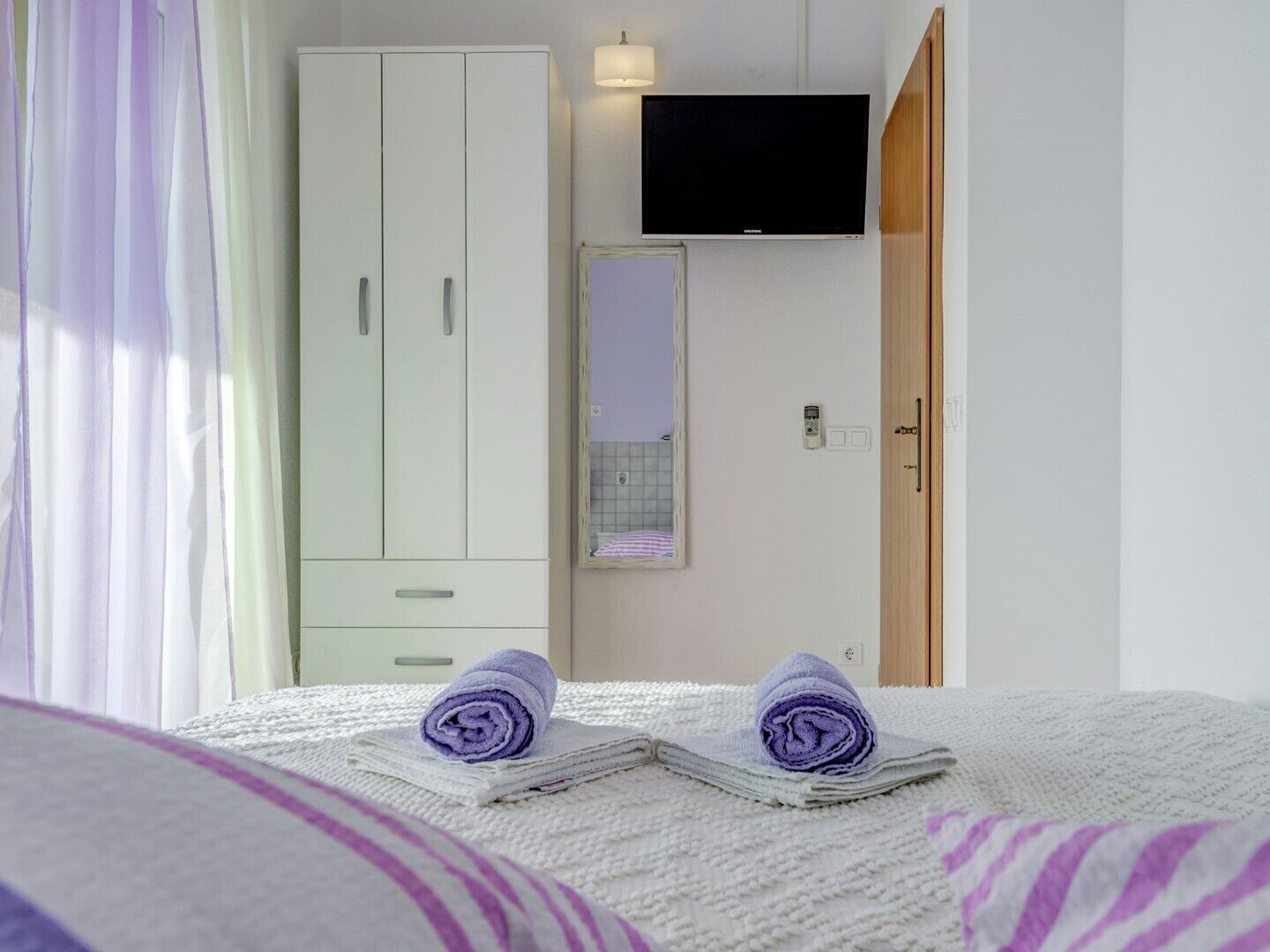 Een hotelkamer met een bed, een kledingkast, een televisie en een spiegel.