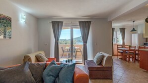 Sala de estar con dos sofás, comedor y cocina. Cuenta con un ventanal corredero que da a un patio exterior.