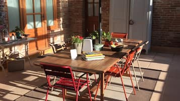 Een terras buiten met een houten tafel en stoelen, een grote parasol en plantenpotten.
