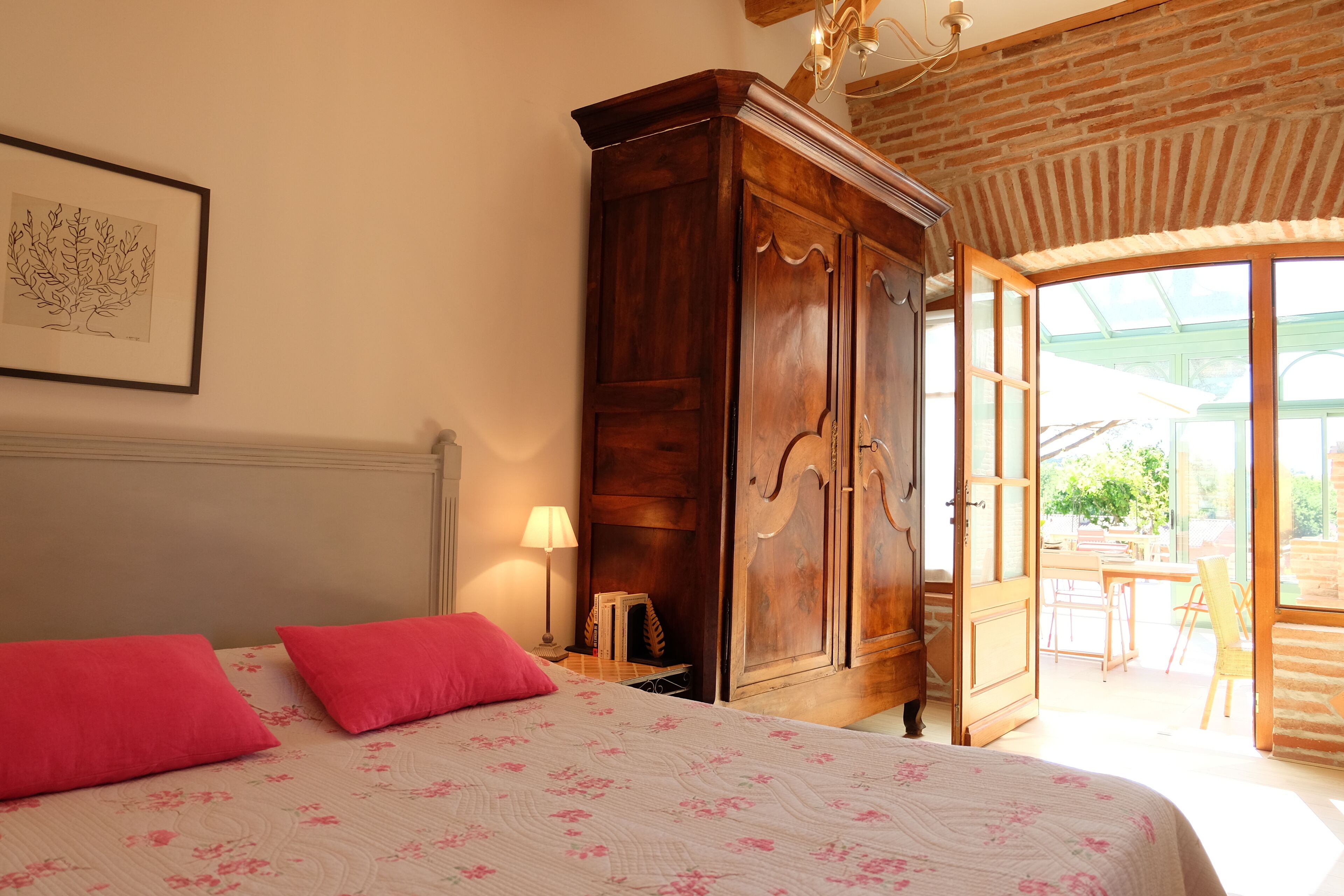 Een slaapkamer met een bed, een houten kledingkast, een lijst met een afbeelding aan de muur en uitzicht op de omgeving.
