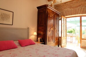 A bedroom with a bed, a wooden wardrobe, a framed picture on the wall, and a view of the outdoors.