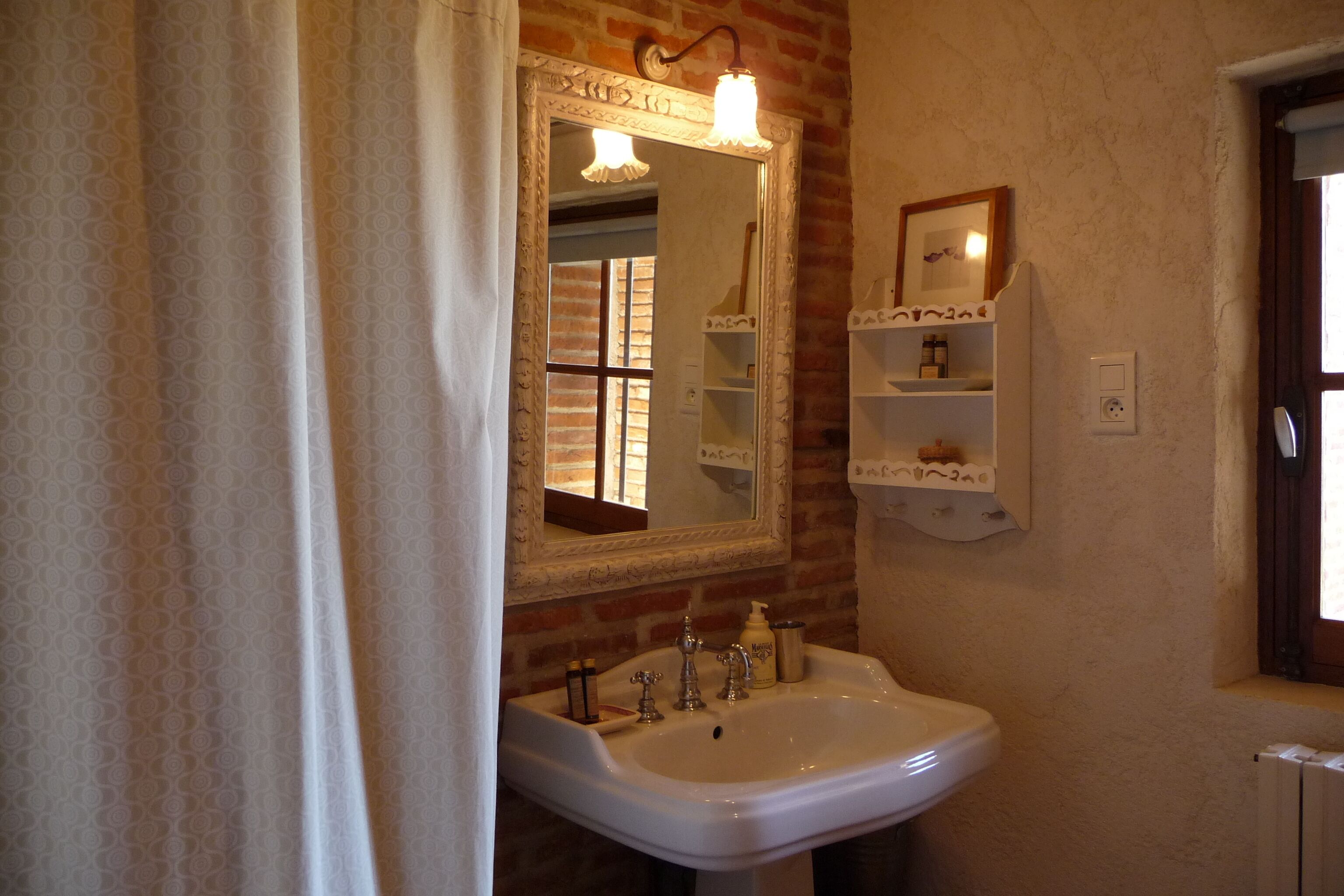 A bathroom with a white sink, a mirror with a light fixture, and a brick wall.