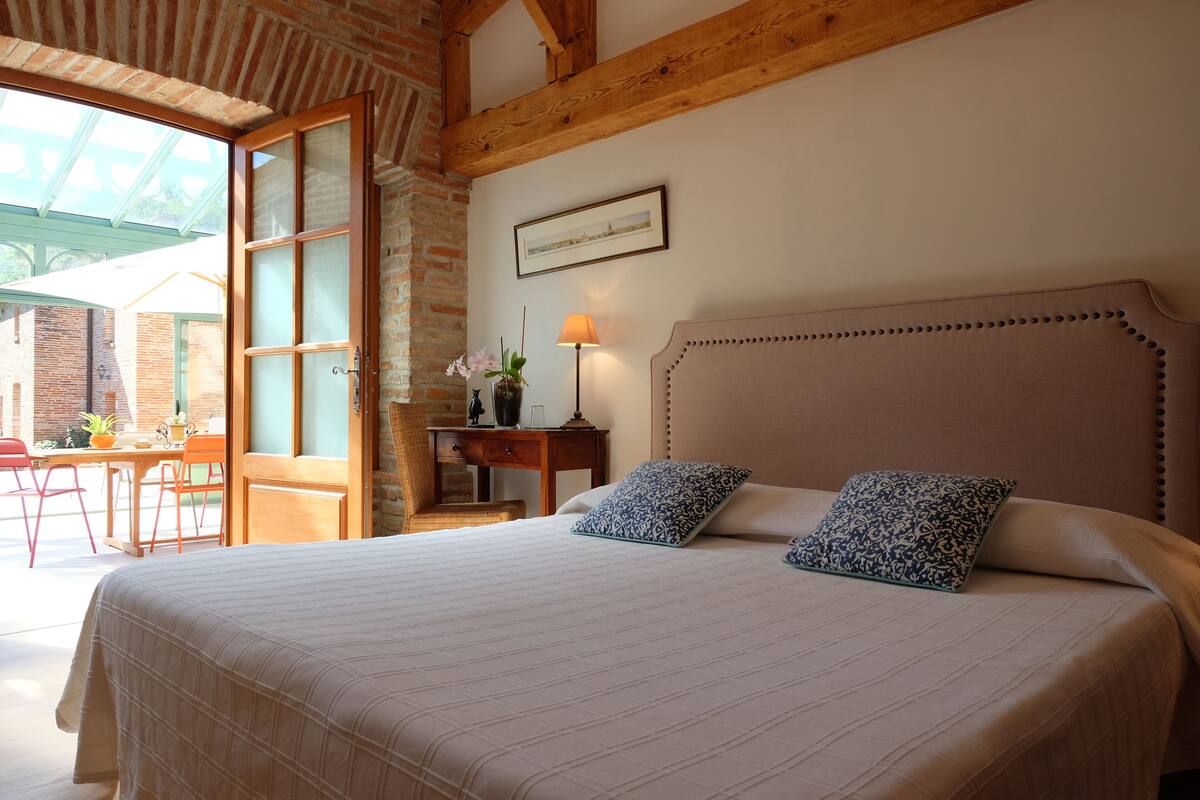 Un dormitorio con una cama grande, cabecera de madera, un escritorio con silla y ventana con vista al exterior.