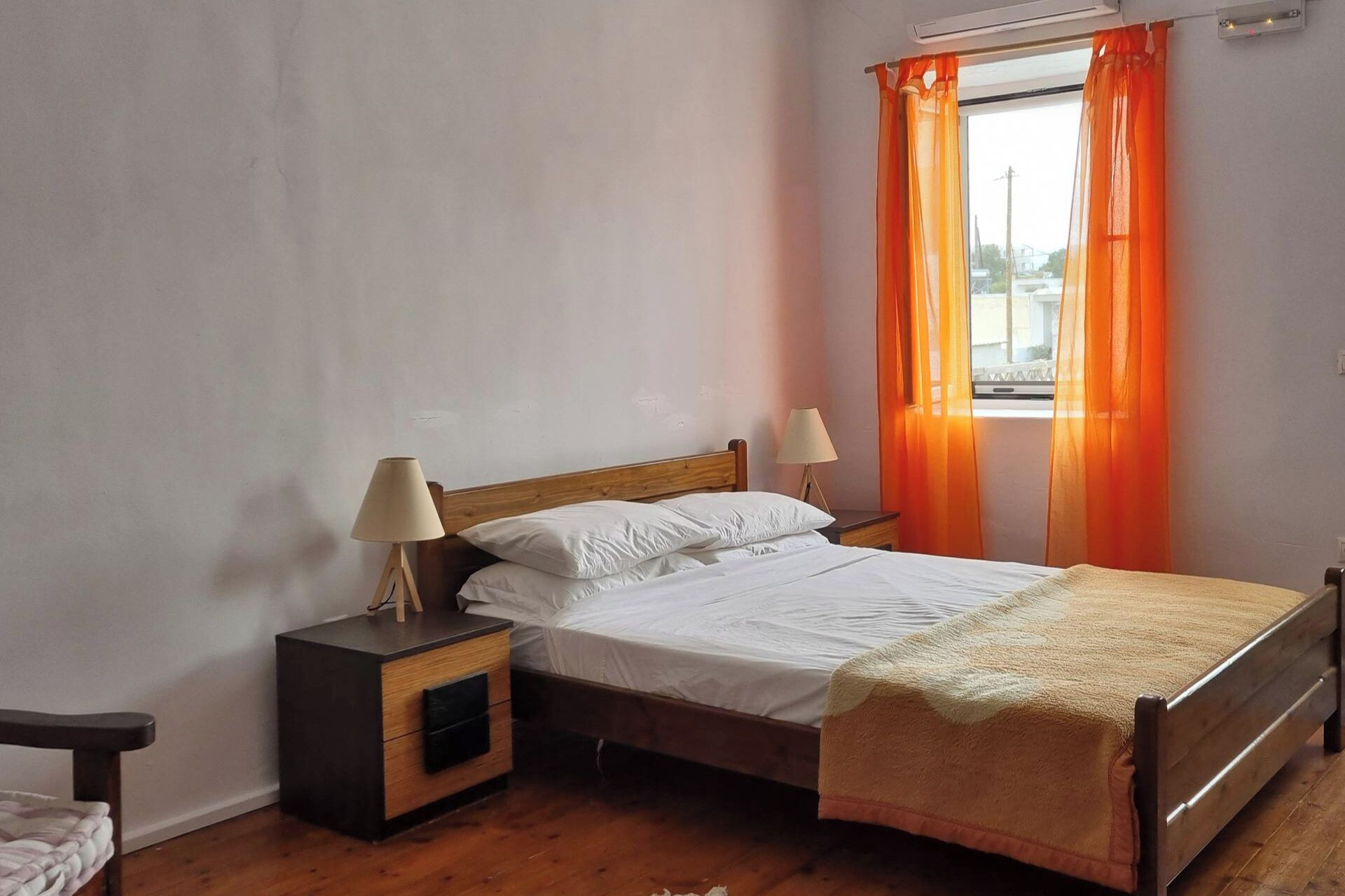 A bedroom with a wooden bed, two bedside tables with lamps, and orange curtains.