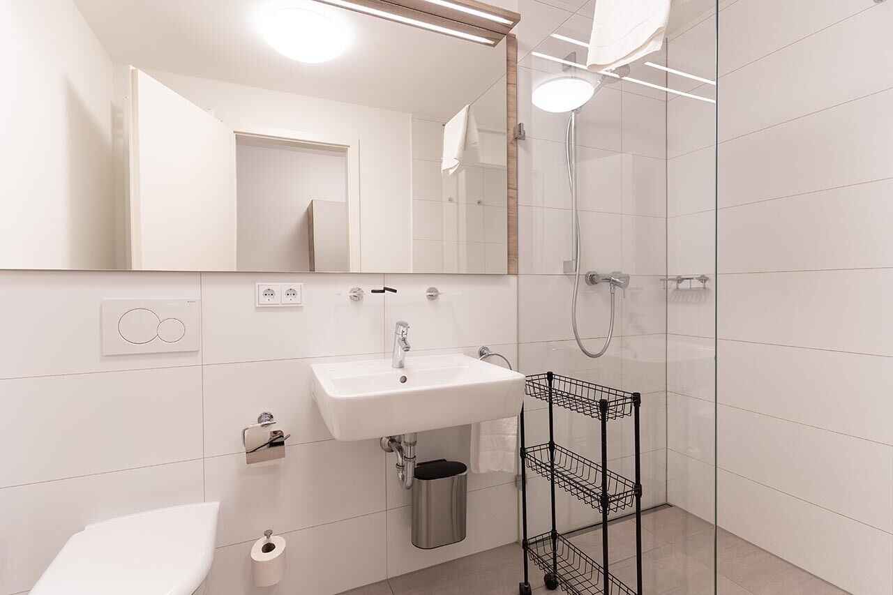 Une salle de bain moderne avec un lavabo blanc, un miroir et une cabine de douche en verre.