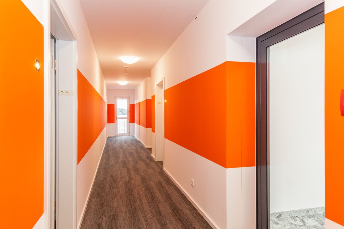 A hallway with alternating orange and white walls, a wooden floor, and a door labeled "D3".