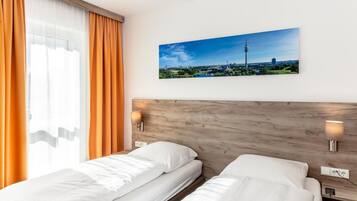 A hotel room with two beds, a wooden headboard, a cityscape painting, and a window with orange curtains.