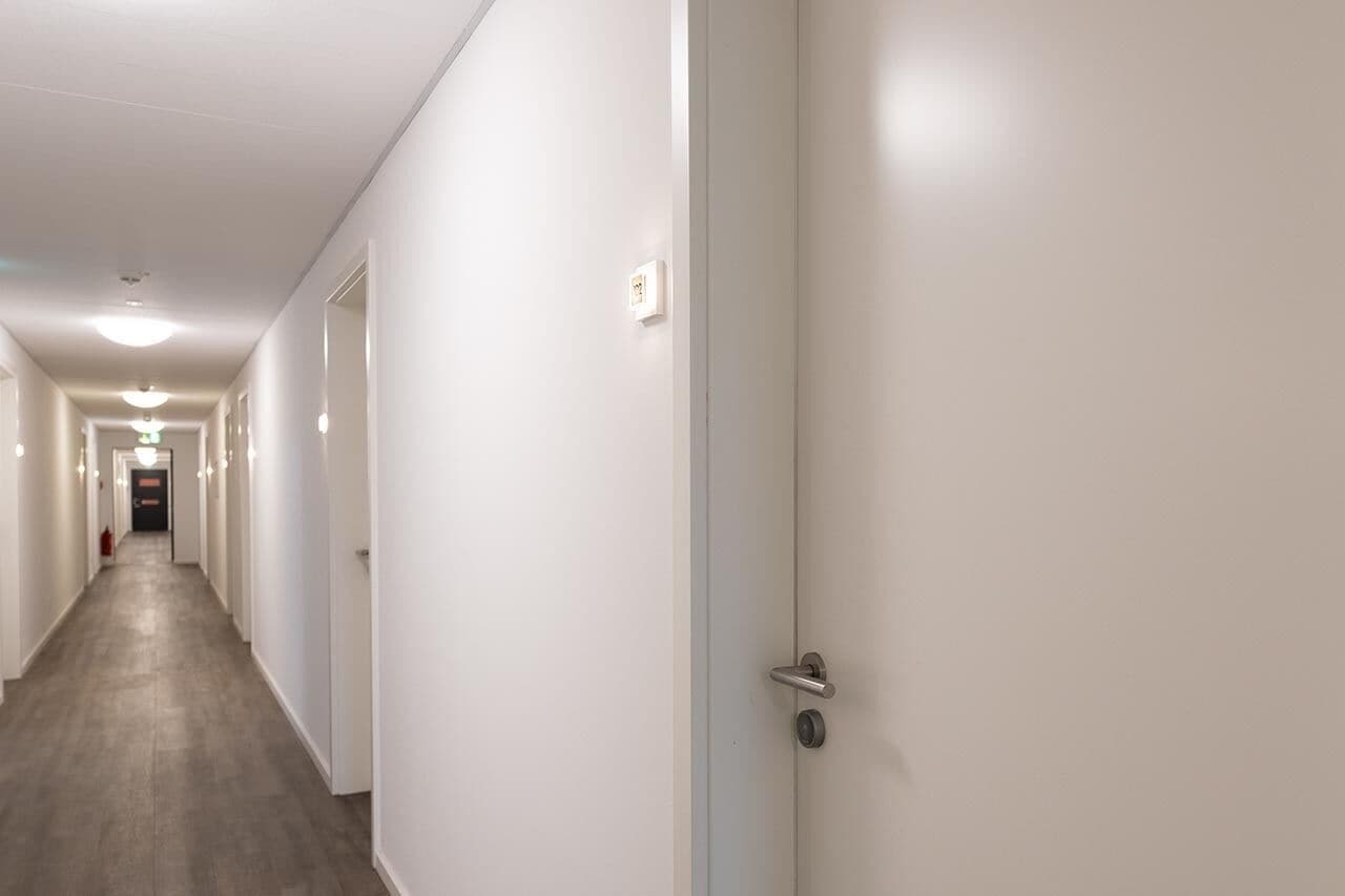 Un largo y estrecho pasillo con paredes blancas y suelo de madera, que conduce a una puerta al final.