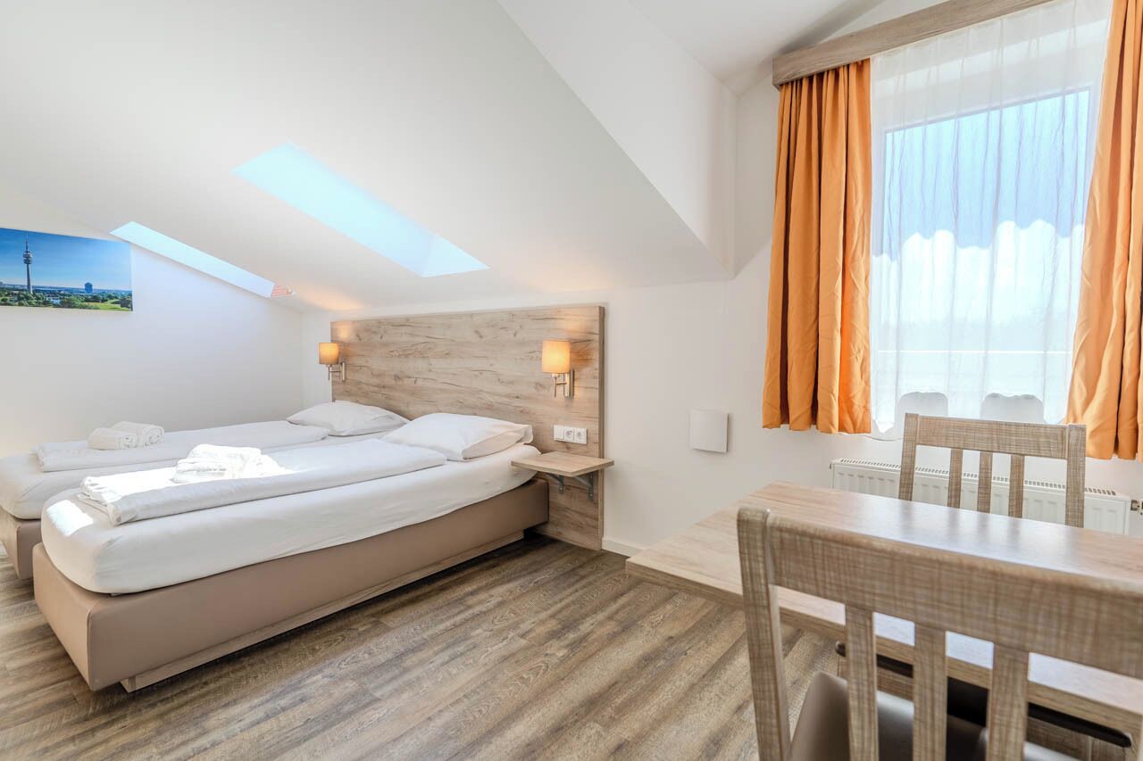 Une chambre d’hôtel moderne, dotée d’un grand lit, d’une table à manger et offrant une vue sur le paysage urbain par la fenêtre.