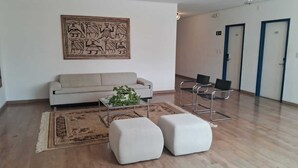 A modern living room with a sofa, two ottomans, a coffee table with plants, and a rug. There are two chairs and a door in the background. - Vitoria Palace Hotel (Lavras)