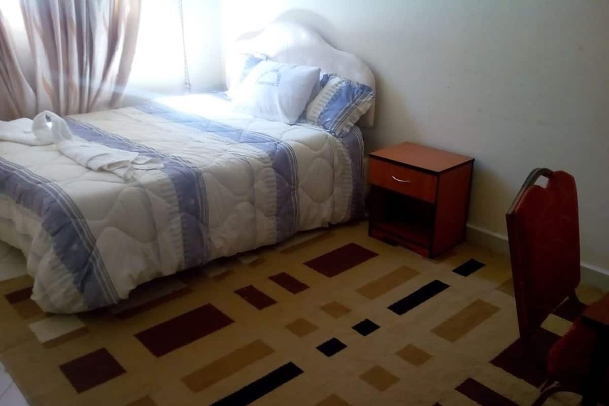 A bedroom with a bed, a nightstand, a chair, and a patterned carpet.