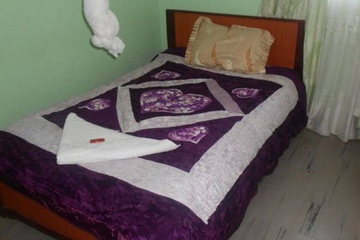 A bed with a purple and white quilt, a wooden headboard, and a white pillow.