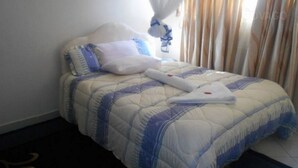 A neatly made bed with a blue and white quilt, a white pillow, and a folded white towel. - Eldoret Adventist Guest House (Eldoret)
