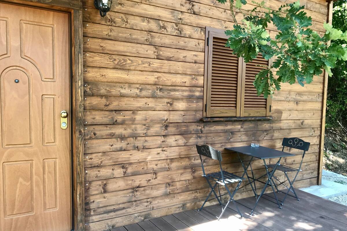 A wooden cabin with a door, a window with shutters, and a small table with chairs outside.