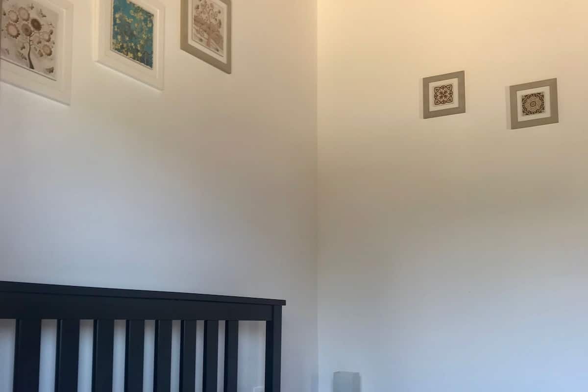 A bedroom with a dark wooden headboard, a bed with striped bedding, a nightstand with a lamp, and three framed pictures on the wall.
