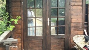 A wooden cabin with a double door, a small porch, and a wicker chair.