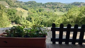 A terrace with a wooden bench and a potted plant, overlooking a lush valley with scattered houses.