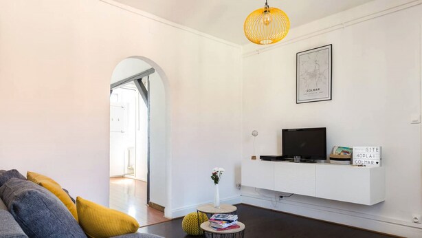 Ein modernes Wohnzimmer mit einem grauen Sofa, einem kleinen runden Tisch mit Büchern, einer weißen Unterhaltungseinheit und einer hängenden Leuchte.