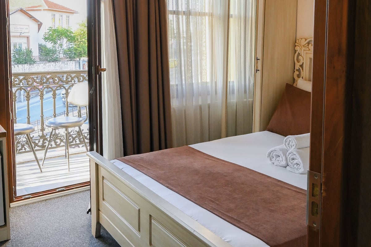 Ein Schlafzimmer mit Bett, Kleiderschrank, einem Balkon mit Stühlen und Blick auf Gebäude.