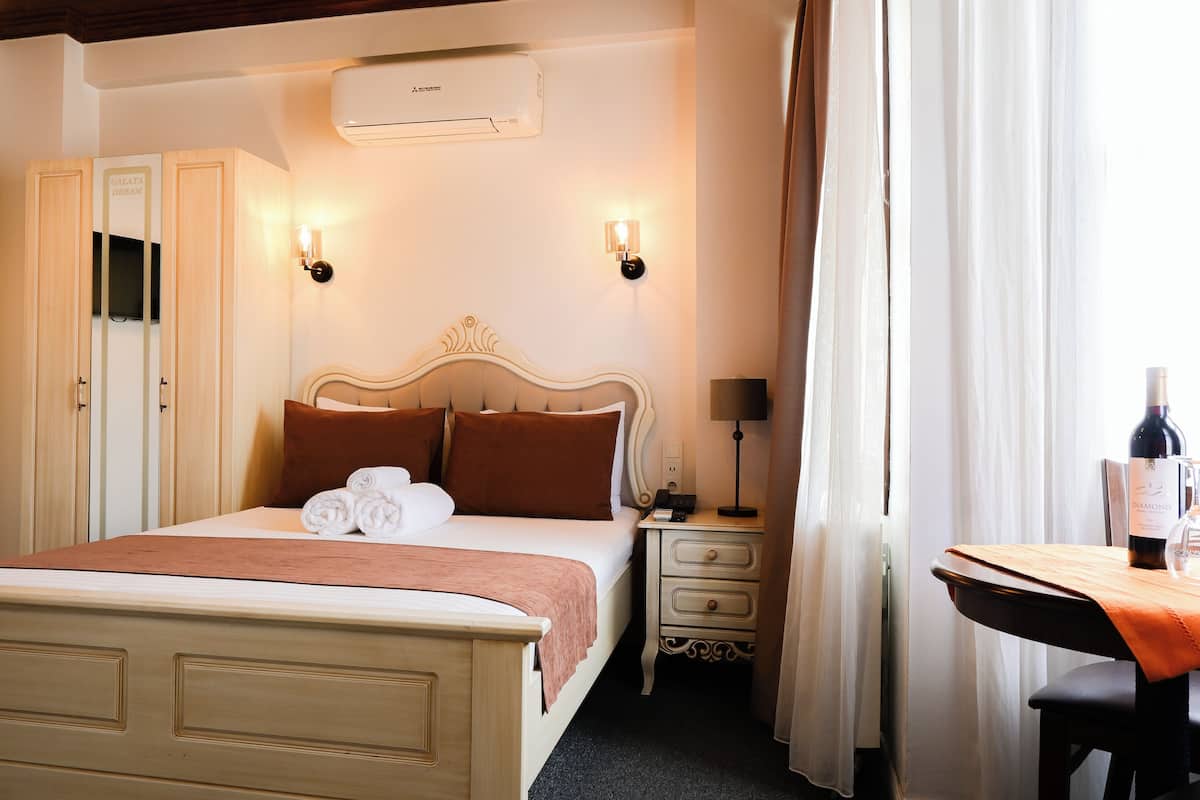Ein Hotelzimmer mit einem Bett, Nachttischen, einem Schreibtisch mit Stuhl und einer Weinflasche.