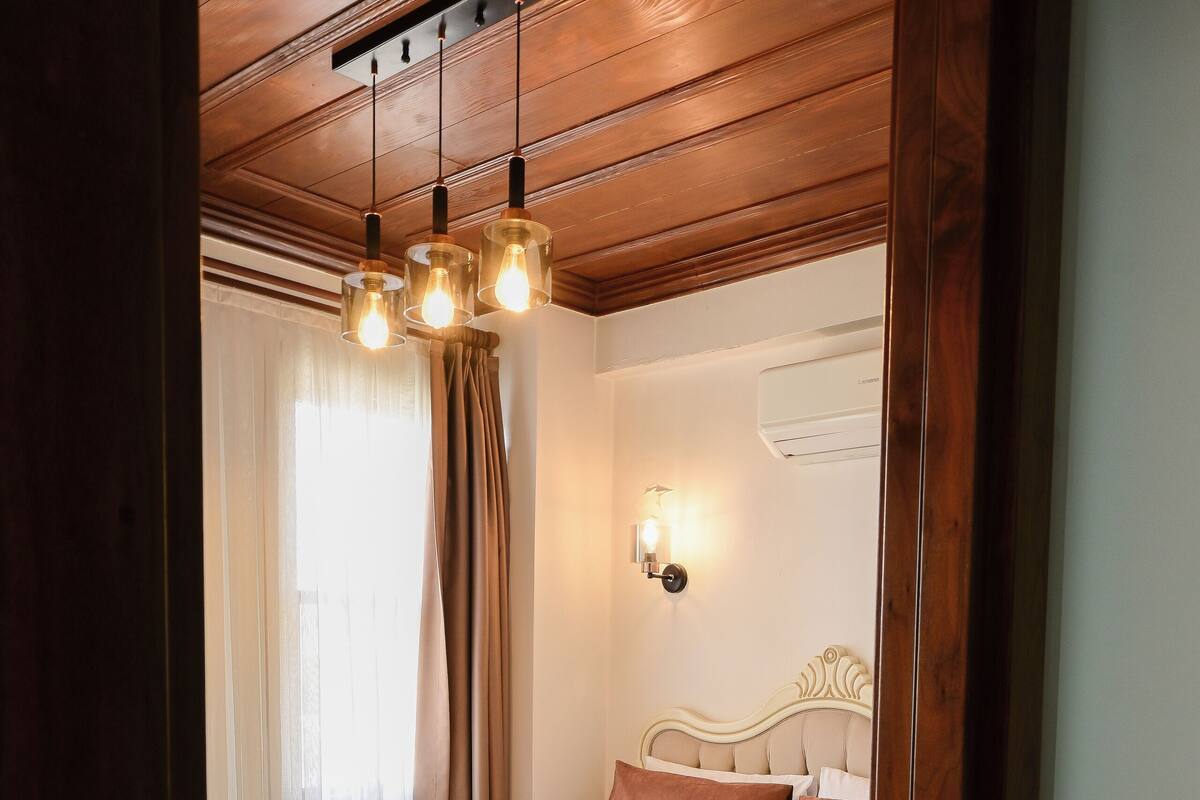 Ein Schlafzimmer mit einem Bett, einer Holzbalkendecke, einer Wandklimaanlage und einem Fenster mit Vorhängen.