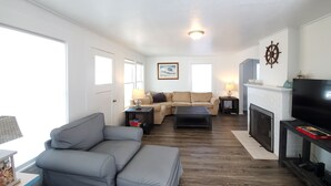 A living room with a grey sofa, a beige sectional, a fireplace, and a television. - Enjoy This 4 Bedroom w/ a Beautiful Yard, Ocean Views and Easy Beach Access! (Seaside)