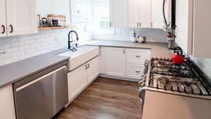 A modern kitchen with white cabinets, a stainless steel dishwasher, a gas stove, and a red kettle. - Enjoy This 4 Bedroom w/ a Beautiful Yard, Ocean Views and Easy Beach Access! (Seaside)