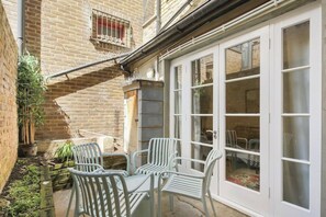 A patio with white plastic chairs and a table, a brick wall, and a sliding glass door leading to an interior space.