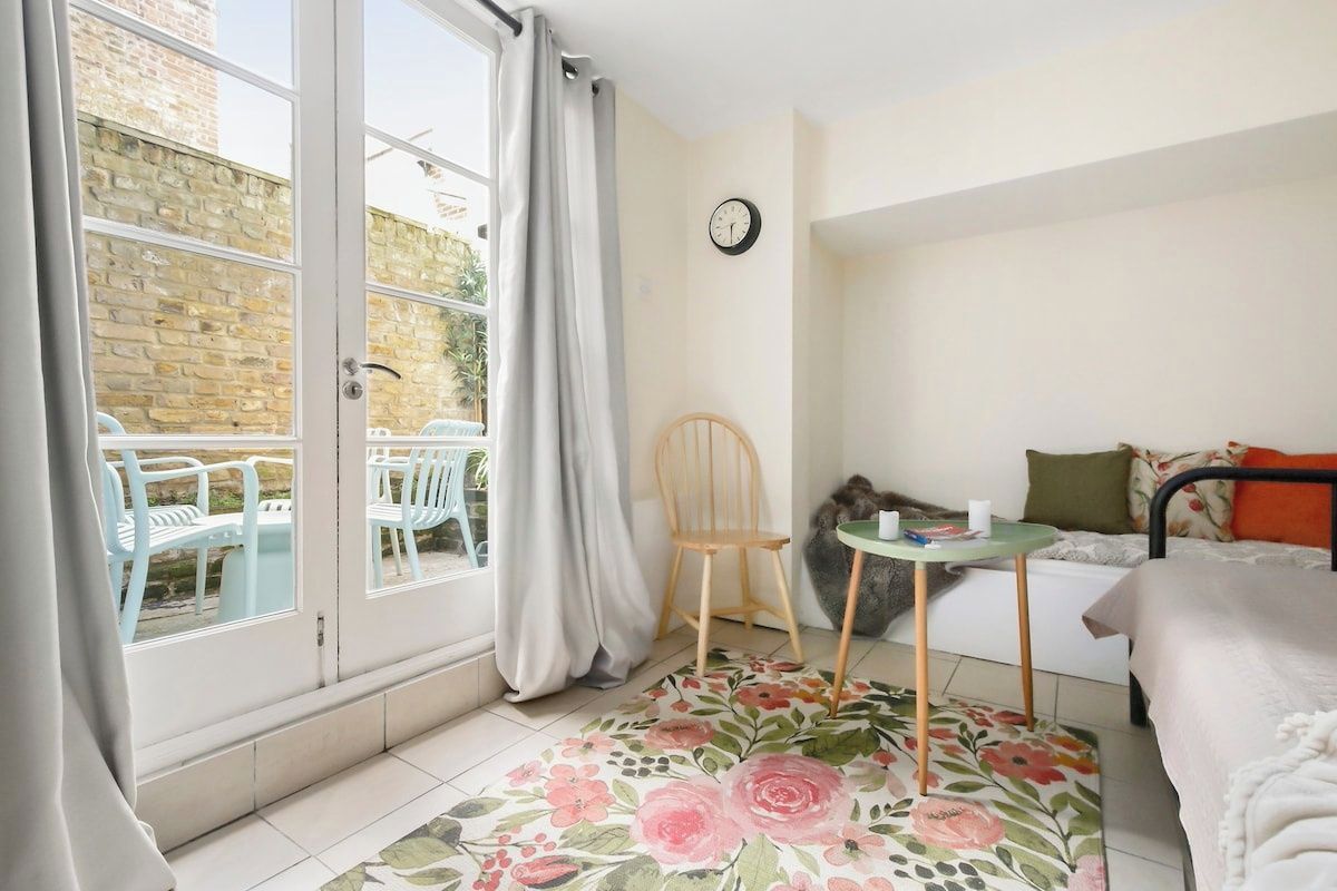 Una habitación con cama, una mesita, una silla y una ventana con vistas a muebles de exterior.