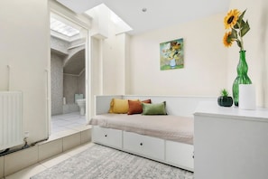 A modern bedroom with a skylight, a bed with multiple pillows, a painting on the wall, and a vase with sunflowers.