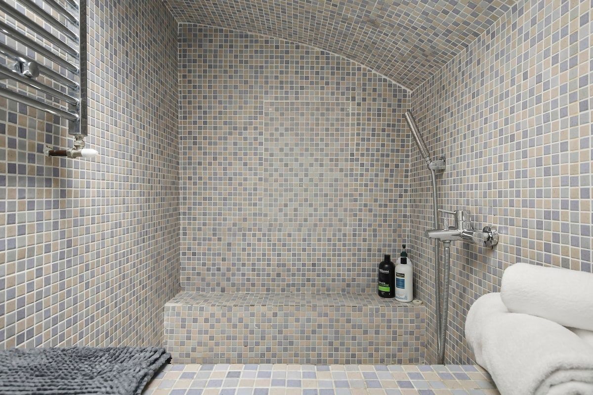 Eine geflieste Dusche mit gewölbter Decke, einer Handbrause und einem Ablagebereich für Toilettenartikel.