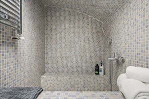 Ducha con azulejos, techo curvo, cabezal de ducha manual y repisa con artículos de aseo.