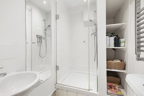 Un baño moderno con ducha envuelta en vidrio, un lavabo blanco y repisas con artículos de aseo.