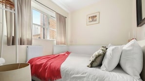 Una camera da letto con un letto, una finestra con tende, un termosifone e un quadro appeso al muro.
