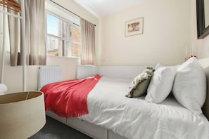 Un dormitorio con cama, ventana con cortinas, radiador y un cuadro colgado en la pared.