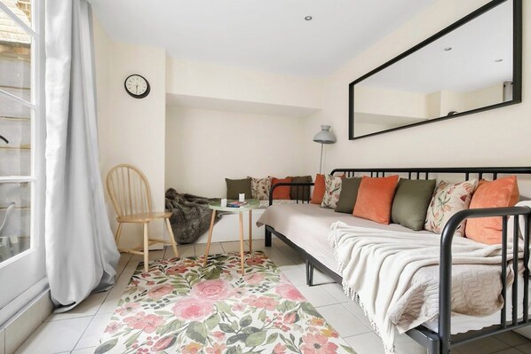 Un dormitorio con cama, una silla, un escritorio, un espejo y una ventana con cortinas.