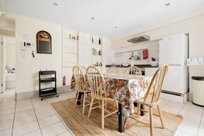 A dining area with a table set for four, surrounded by chairs, a kitchen in the background, and a break sign on the wall.