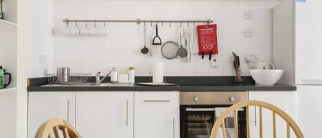 A compact kitchen with white cabinets, a black countertop, and a dining area with a floral tablecloth.