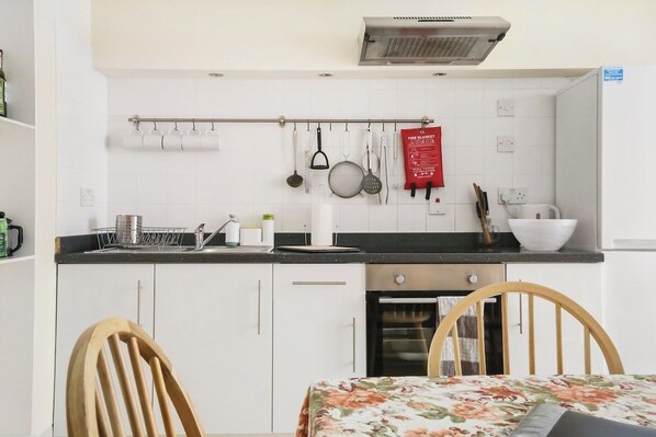 A compact kitchen with white cabinets, a black countertop, and a dining area with a floral tablecloth.