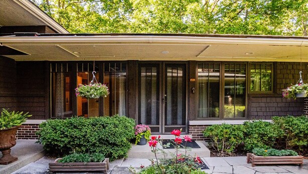 Una casa moderna con un portico coperto, ampie finestre e un giardino curato con diverse piante e fiori.