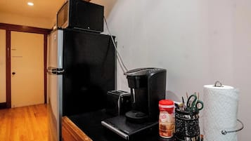 Een kitchenette met een koffiezetapparaat, een blik koffie, een houders voor keukenpapier en een kleine prullenbak.