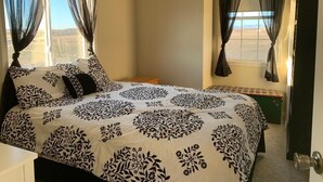A bedroom with a large bed, two windows with sheer curtains, a bedside table, and a view of the outside. - Lovely house on the Snake River that is minutes from CJ Strike Reservoir ! (Bruneau)