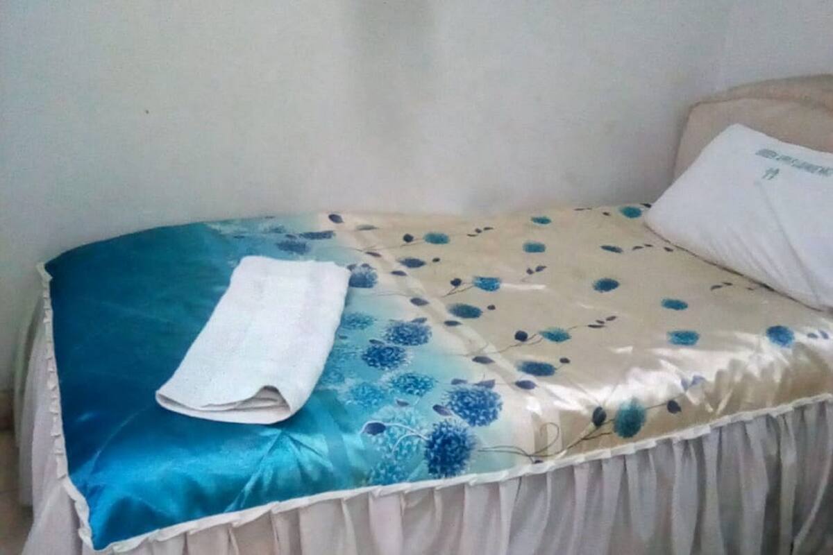 A single bed with a floral bedspread, a white pillow, and a folded white towel.