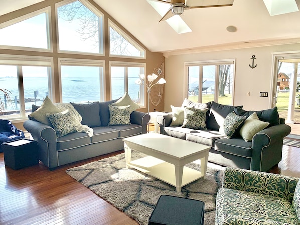 A spacious living room with two sofas, a coffee table, and large windows offering a view of the water. - Beautiful Lakefront Home On Lake St Clair! (Ira)