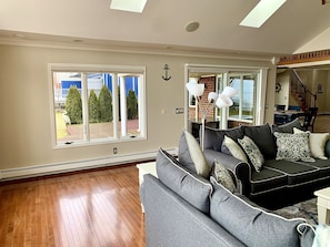 A living room with a gray sofa, a dining area with a table and chairs, and a view of the outside through large windows. - Beautiful Lakefront Home On Lake St Clair! (Ira)