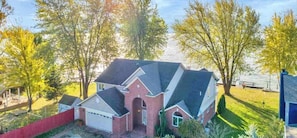 A two-story house with a garage, surrounded by trees and a red fence. - Beautiful Lakefront Home On Lake St Clair! (Ira)
