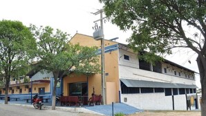 A building with a yellow facade, a covered outdoor seating area, and a staircase leading to a second floor. - Hotel Porto Bello (Caico)