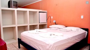 A bedroom with a bed, white pillows, and a TV on a shelf. - Hotel Porto Bello (Caico)